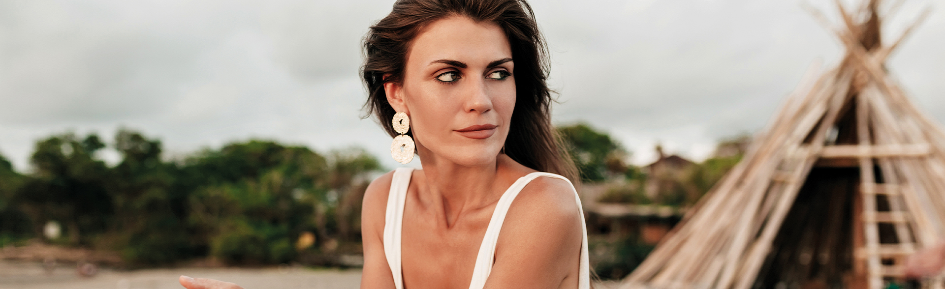 Frau mit langen braunen Haaren und weißem Top sitzt im Freien.